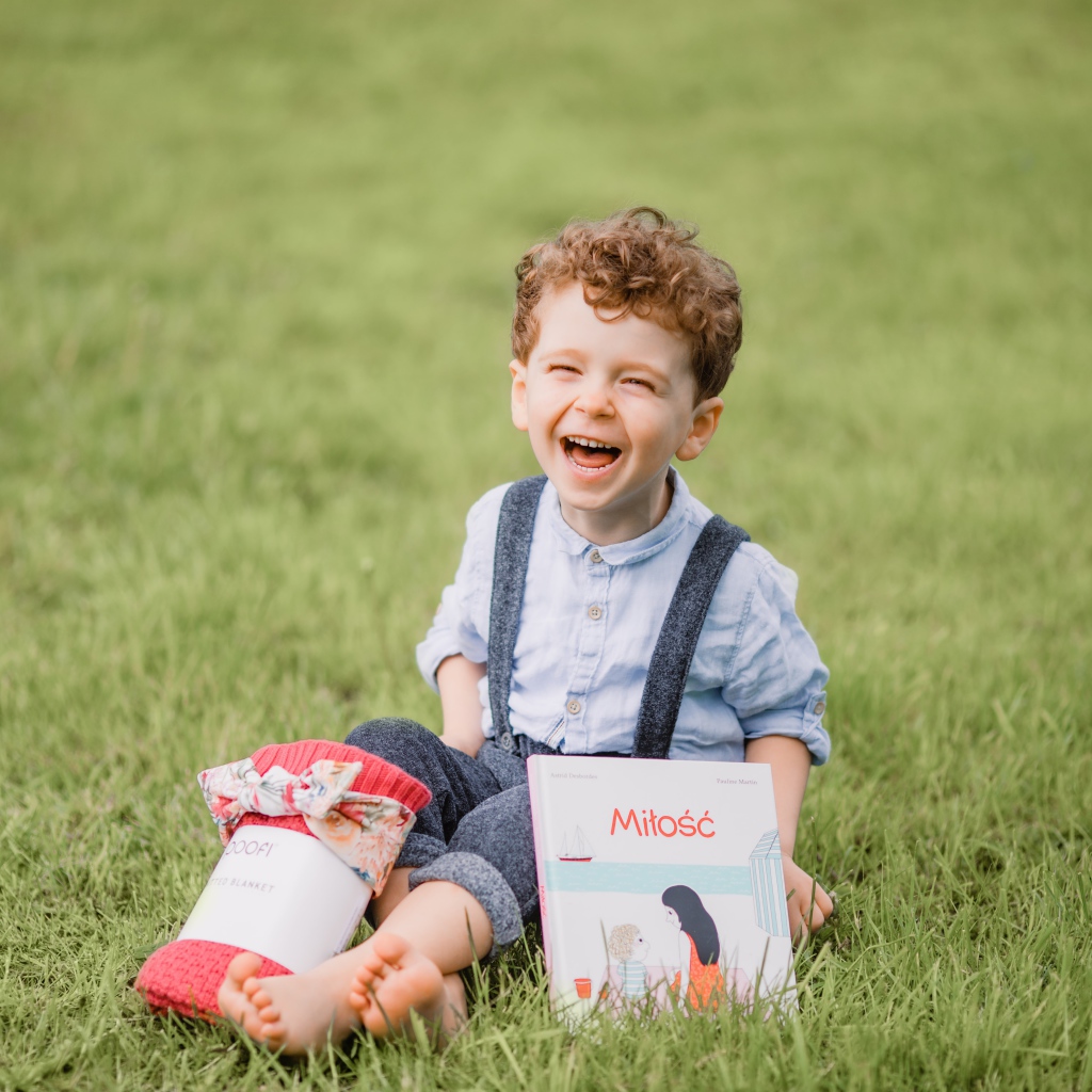Маленький улыбающийся мальчик сидит на зеленой траве с книгой 