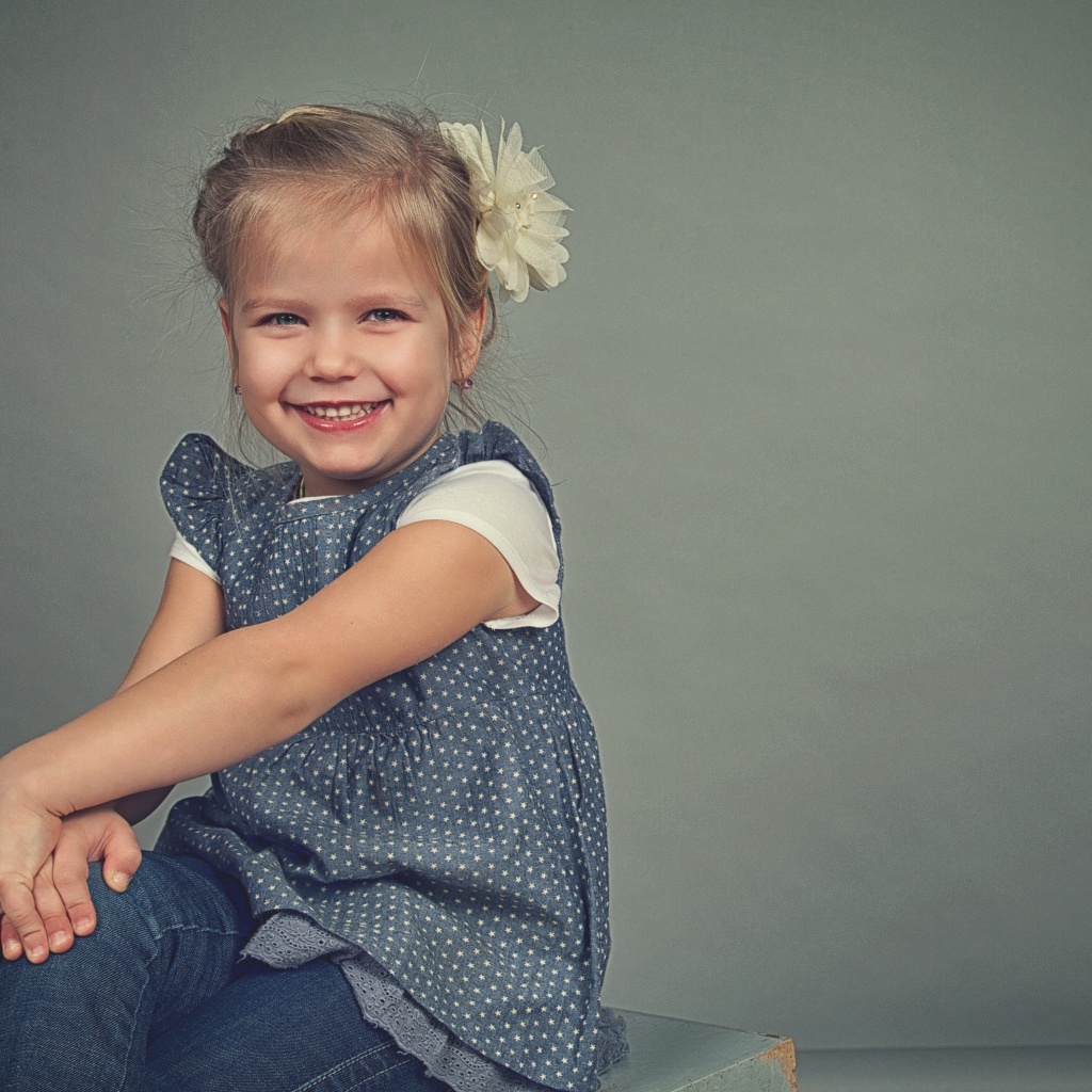 Маленькая улыбающаяся девочка с бантом на сером фоне 