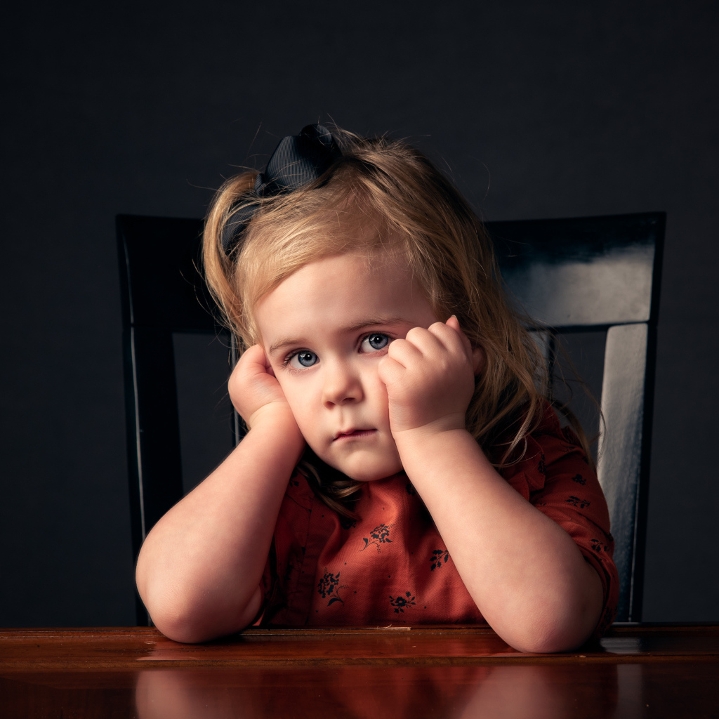 Грустная маленькая девочка сидит за столом