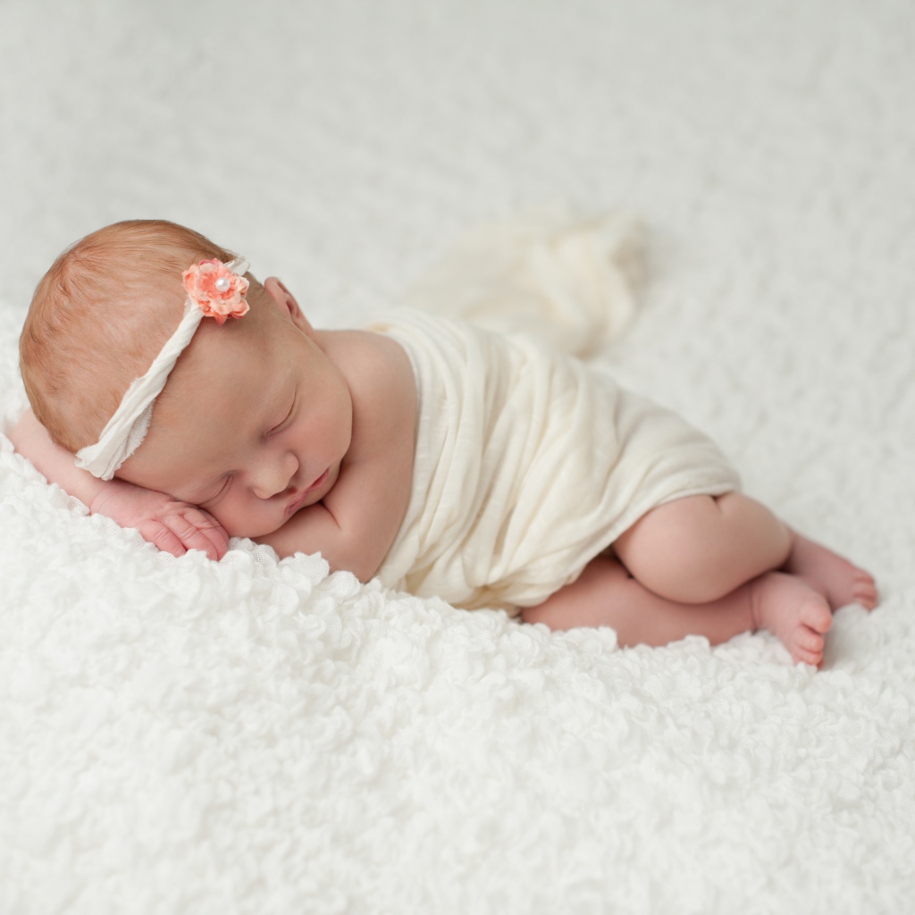 Маленький грудной ребенок спит на белом покрывале 