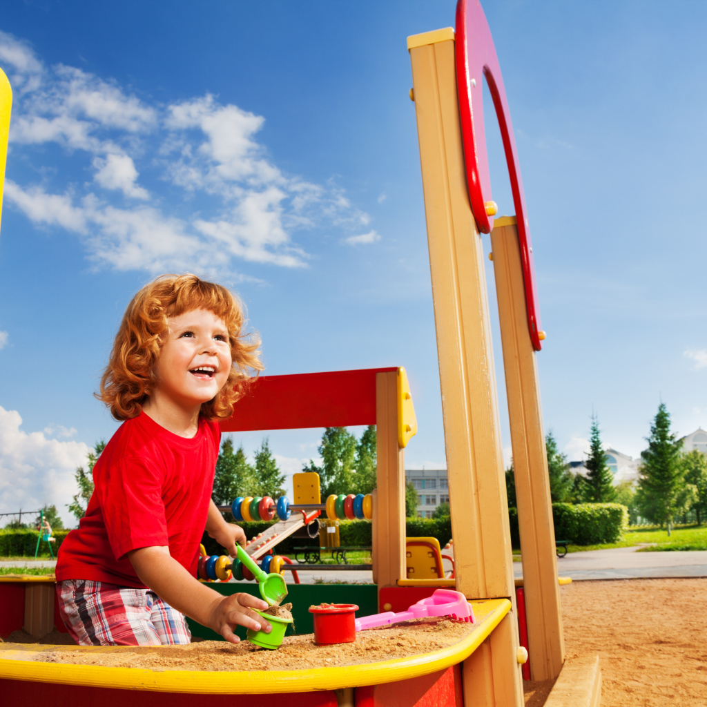 Улыбающийся мальчик в песочнице на детской площадке 