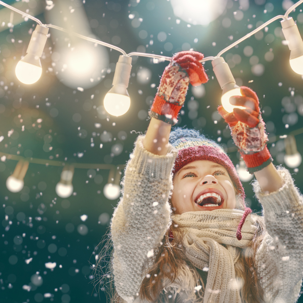 Улыбающаяся девочка вешает лампочки 