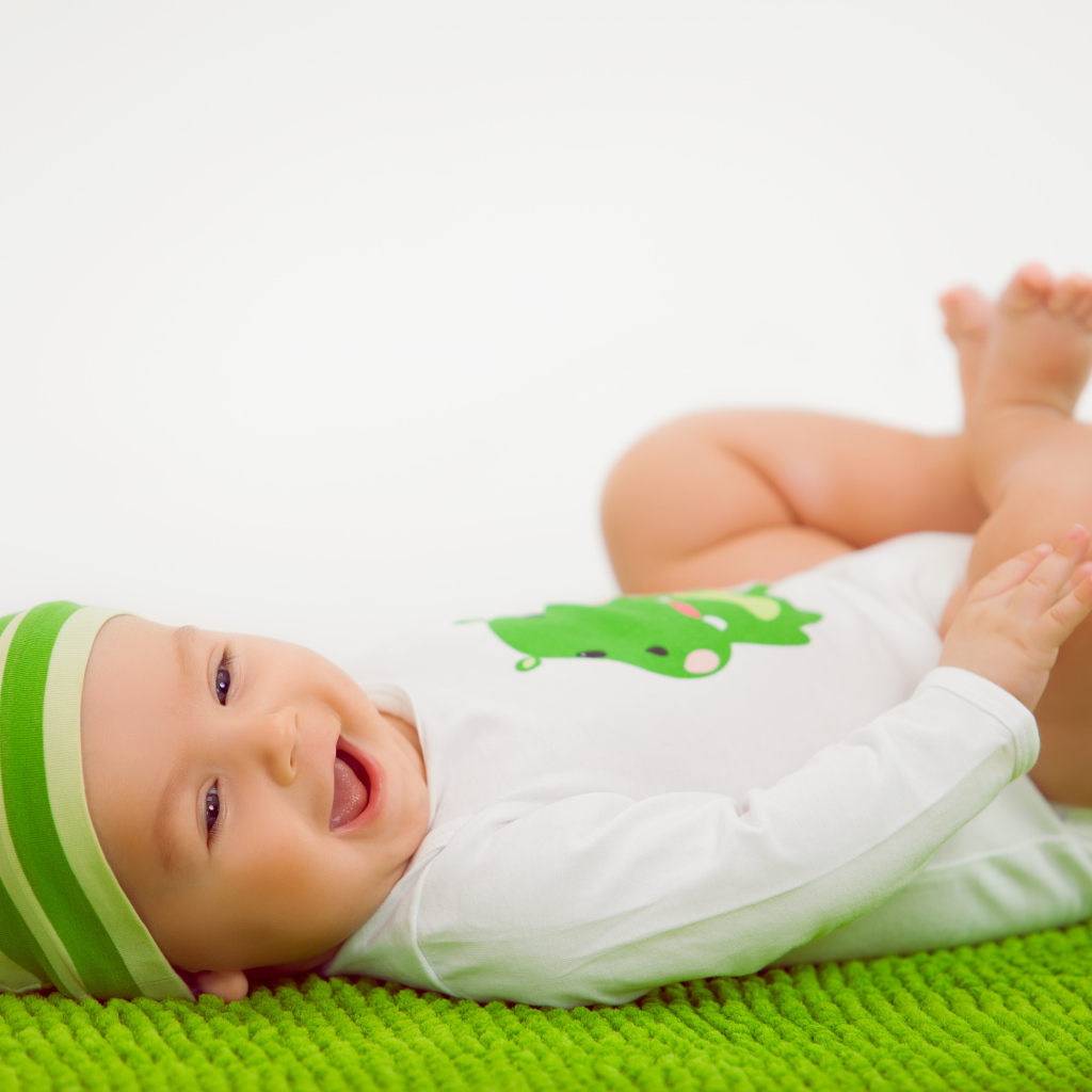 Улыбающийся маленький ребенок лежит на зеленом покрывале 