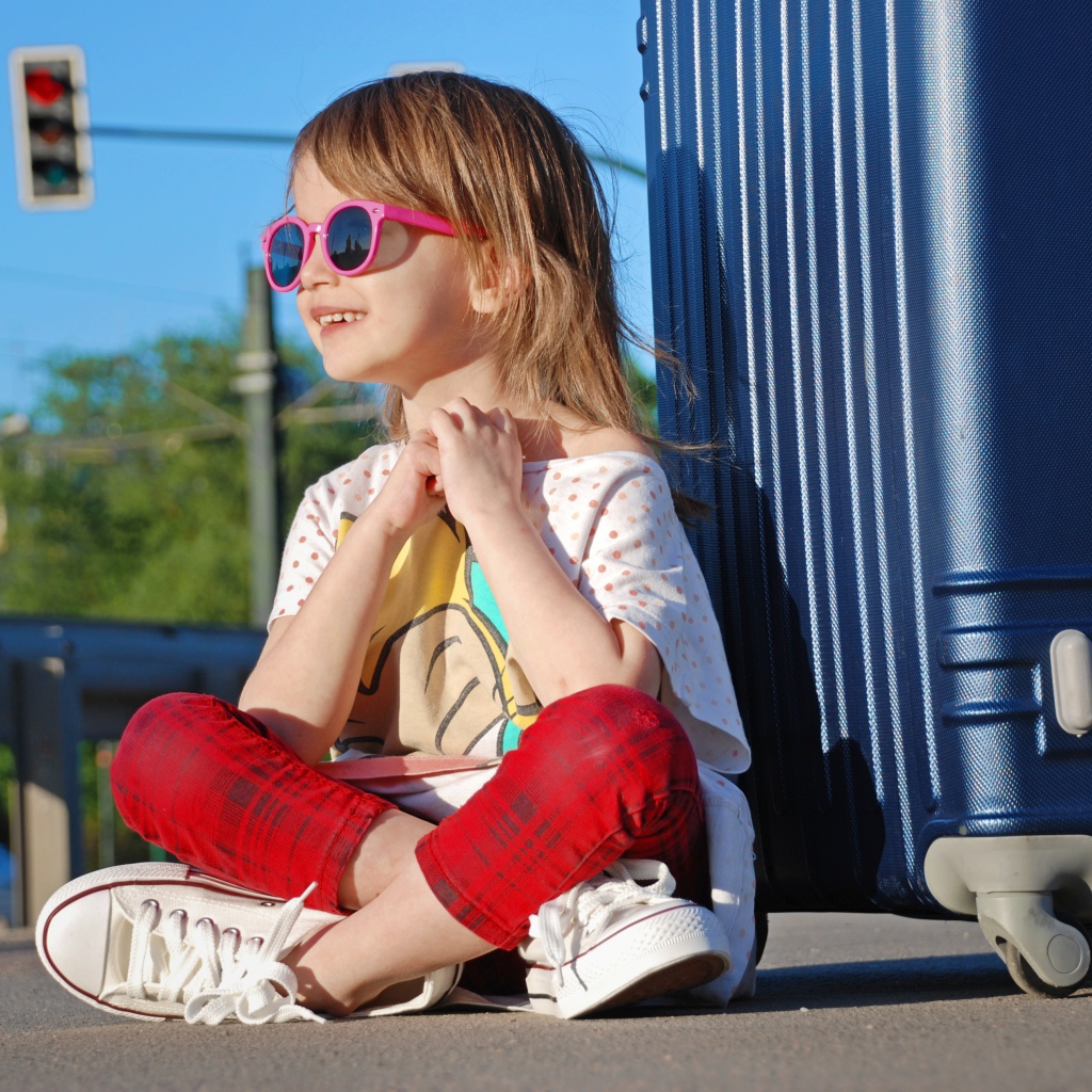 Улыбающаяся маленькая девочка в очках с чемоданом
