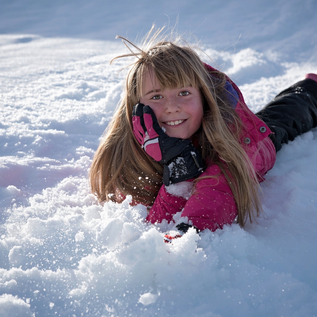 Улыбающаяся маленькая девочка лежит на снегу