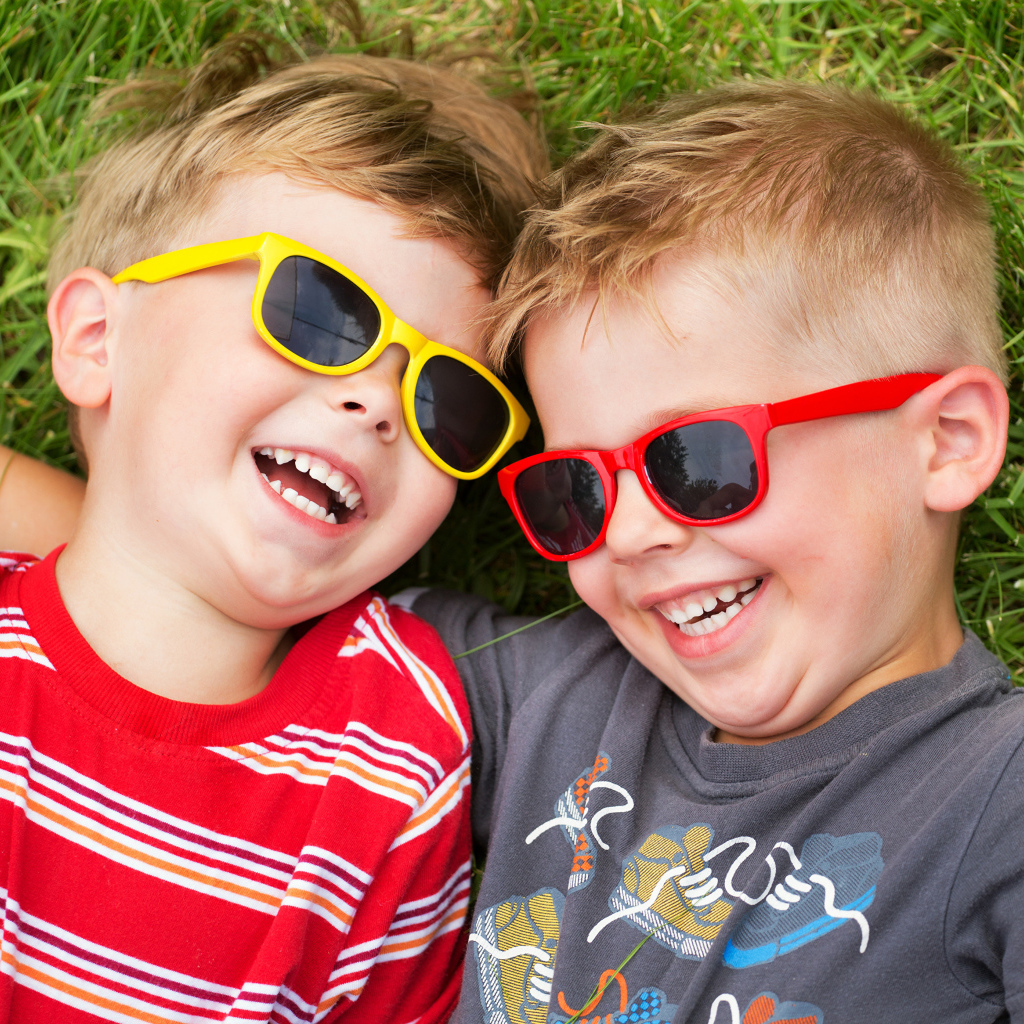 Два улыбающихся мальчика в очках на зеленой траве 