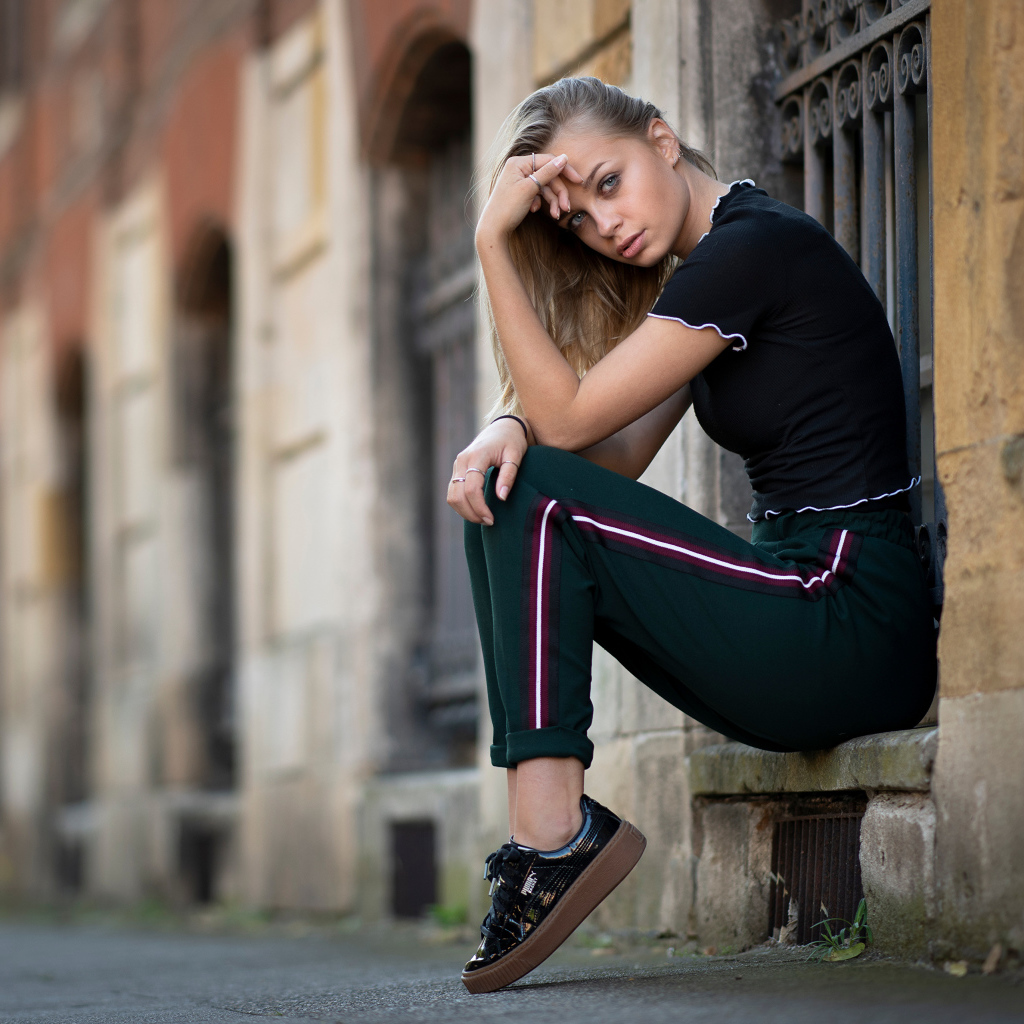 Девушка в спортивном костюме сидит у здания
