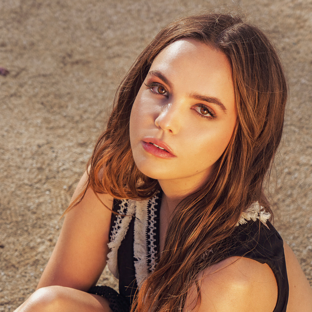 Кареглазая актриса Бэйли Мэдисон сидит на песке