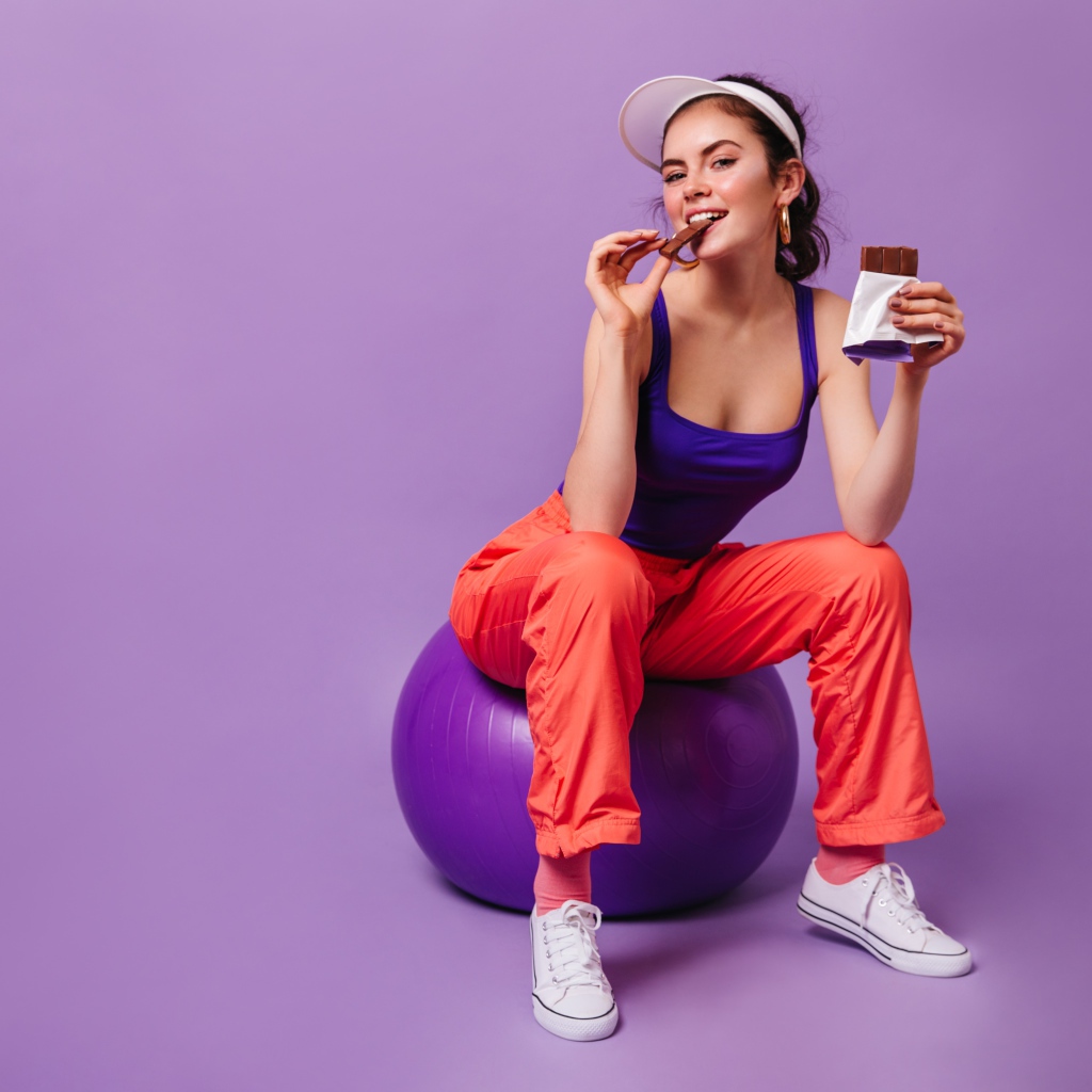 Девушка с шоколадкой сидит на фитболе