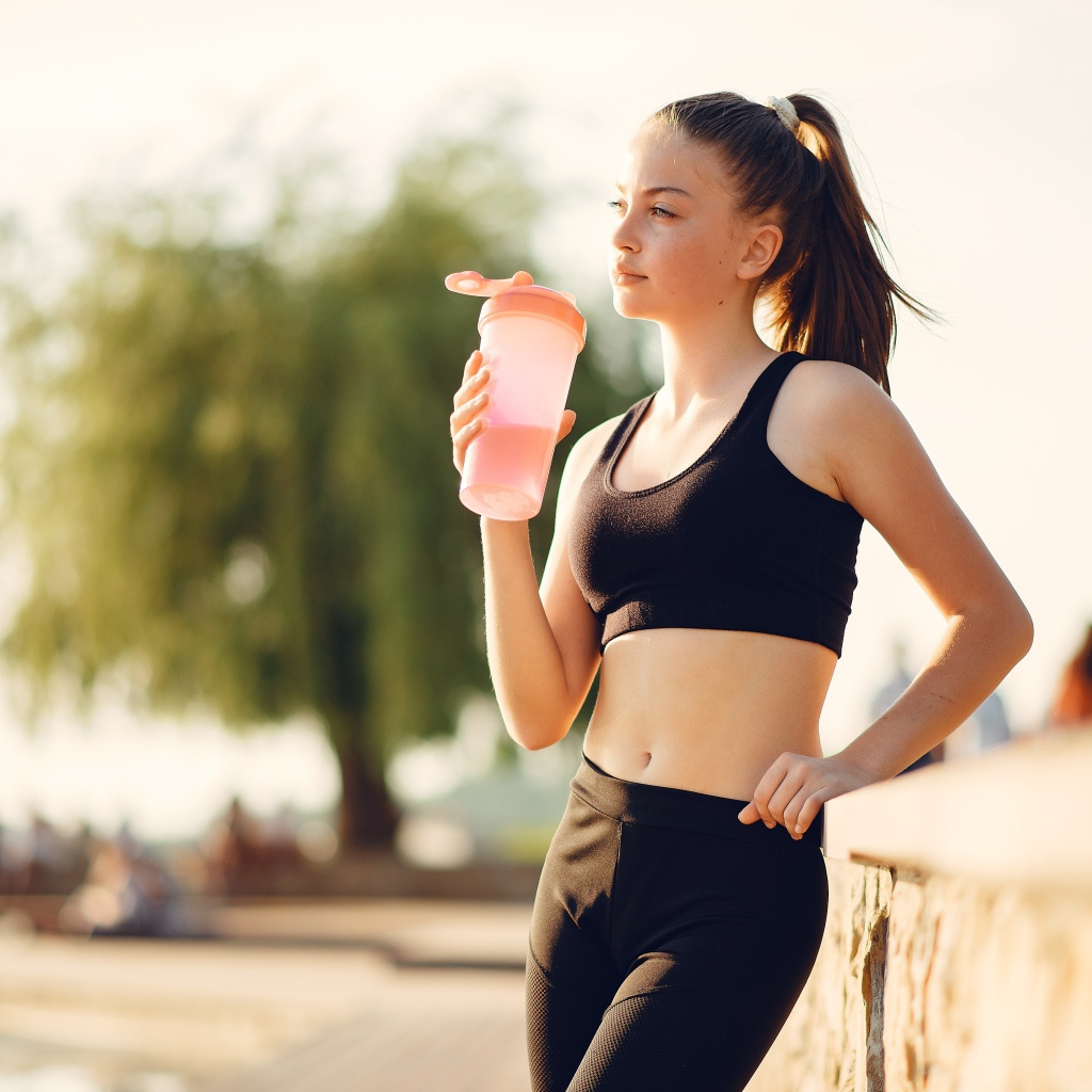 Спортивная девушка в черном пьет воду