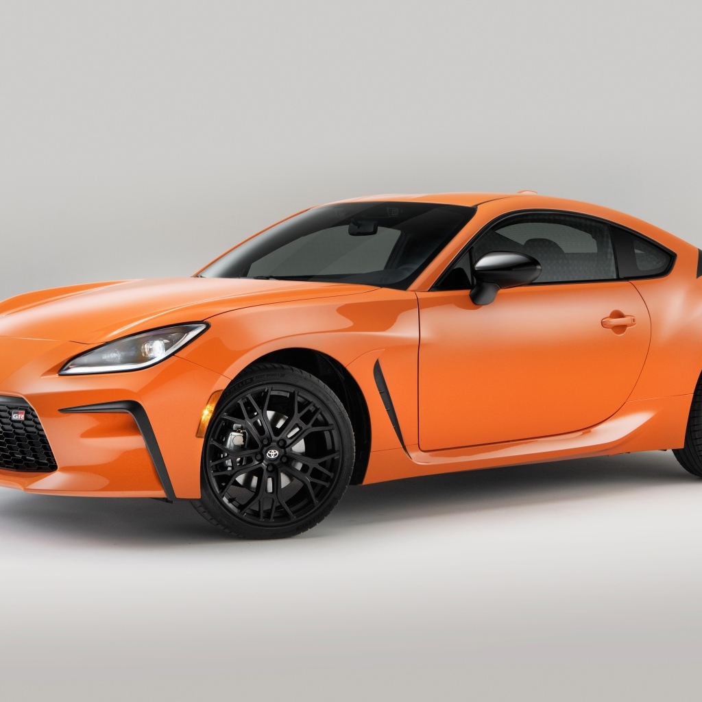 Оранжевый автомобиль Toyota GR 86 на сером фоне