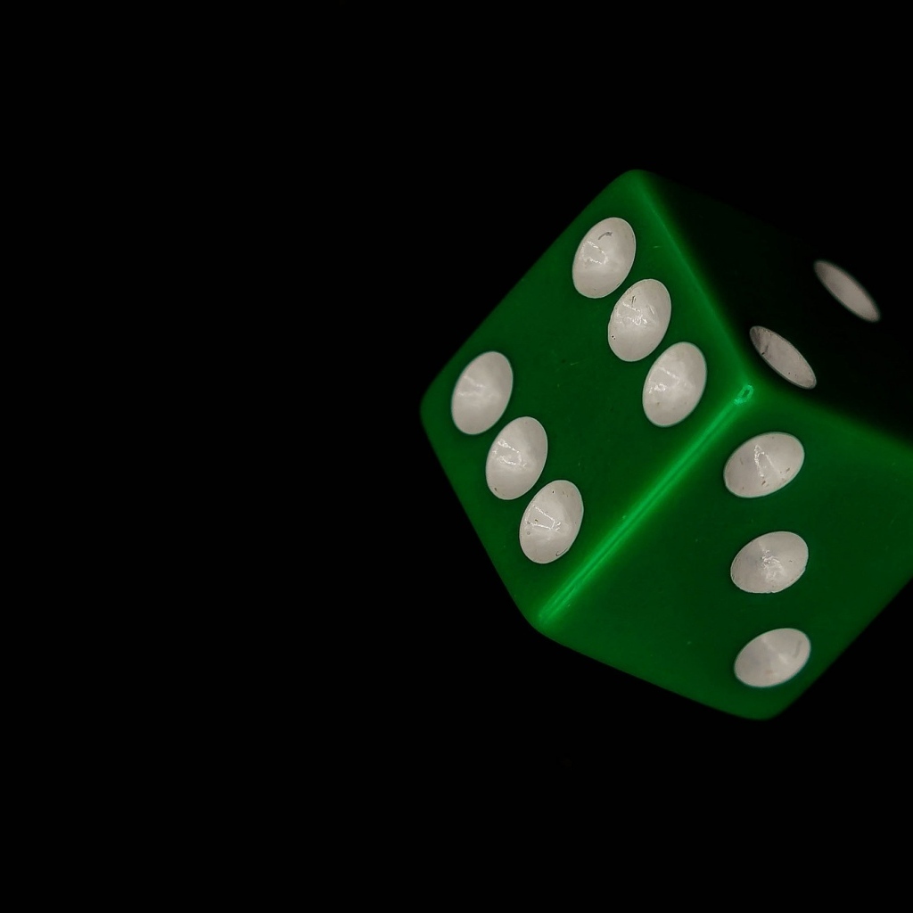 Зеленый игральный кубик на черном фоне