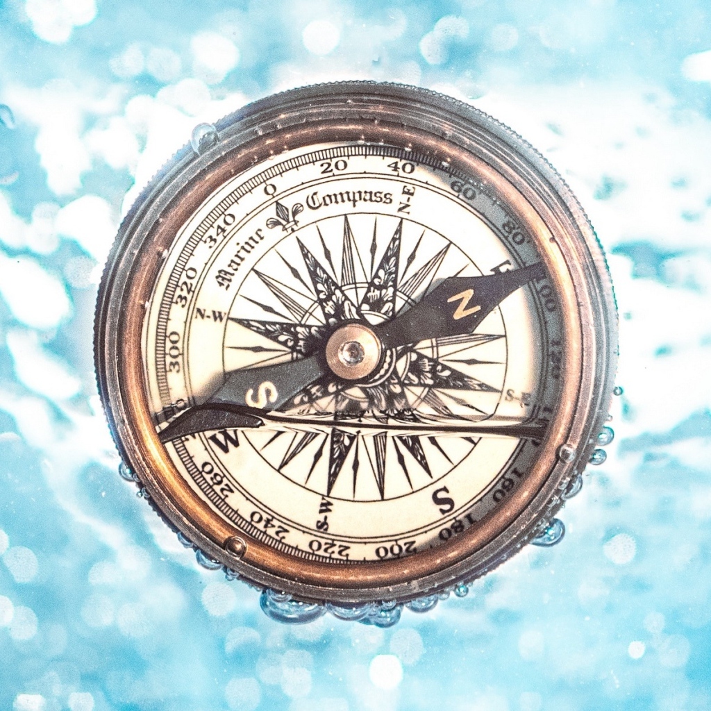 Старый компас в воде на голубом фоне