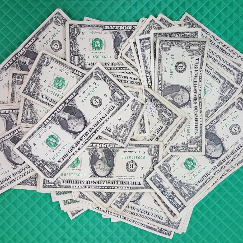 Много купюр в один доллар на зеленой поверхности