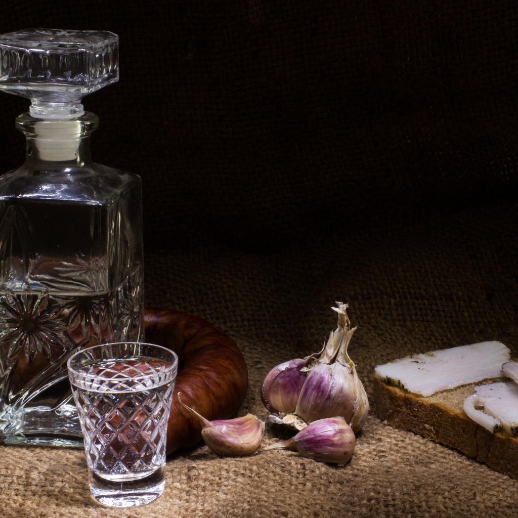 Бутылка водки на столе с салом, колбасой и чесноком