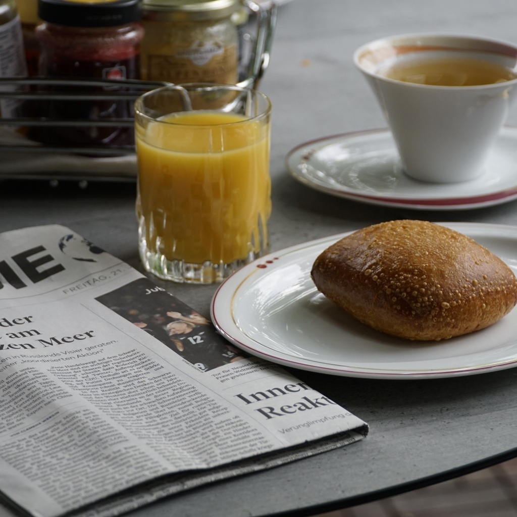 Булочка и стакан сока на столе с газетой