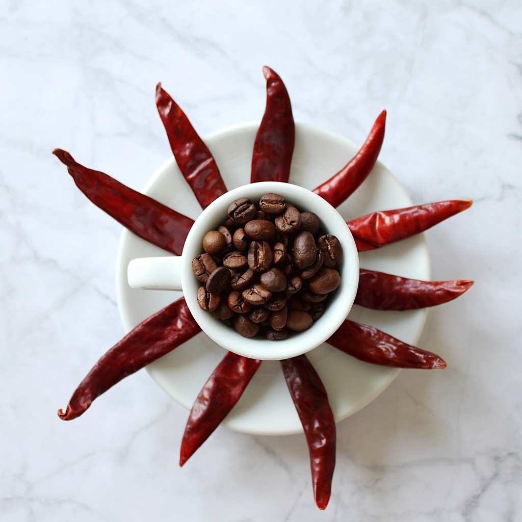 Кофейные зерна в чашке на тарелке с красным перцем