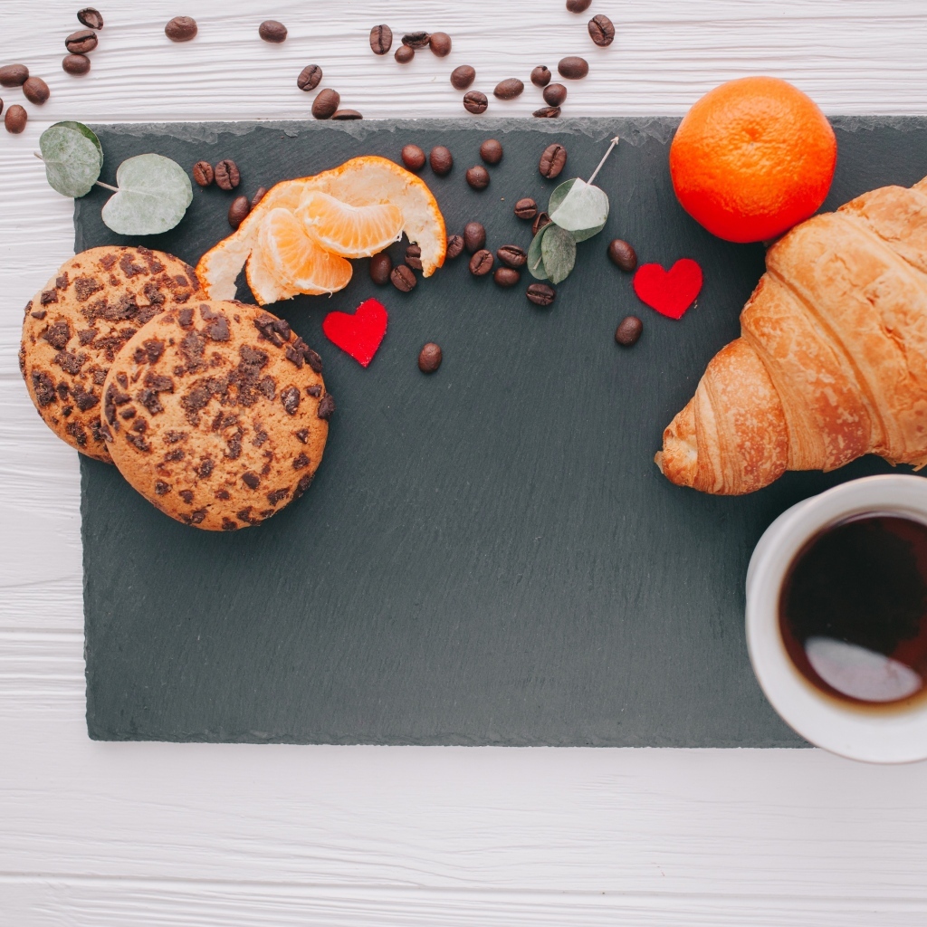 Круассан на столе с печенье, чашкой кофе и мандарином