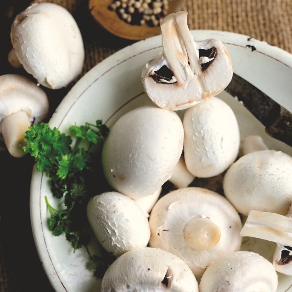 Свежие шампиньоны на тарелке на столе