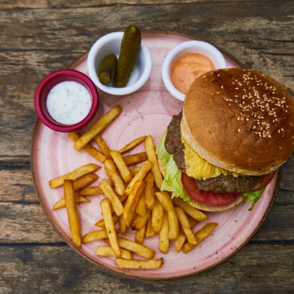 Гамбургер на тарелке с картофелем фри, огурцами и соусом