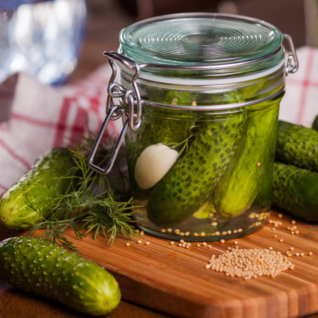 Маринованные огурцы в банке на столе со свежими