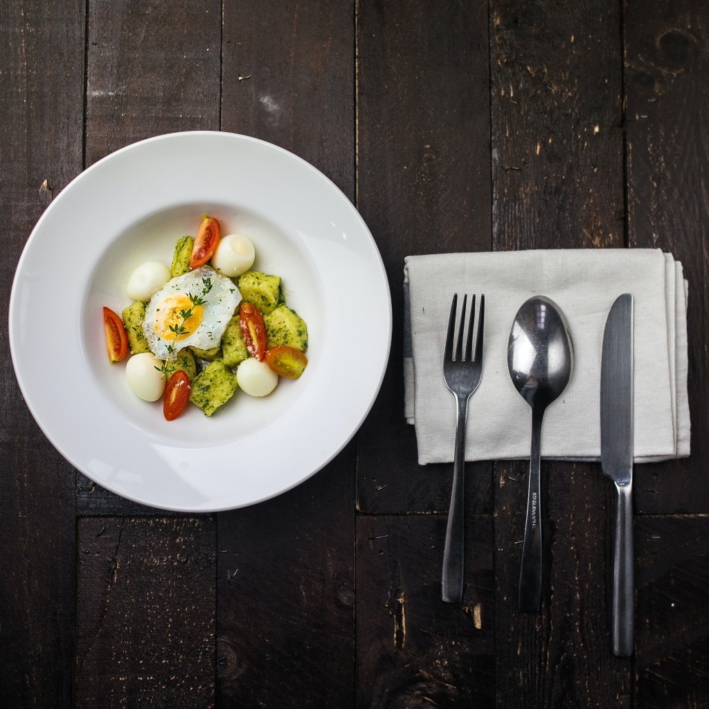 Яичница с овощами в белой тарелке на столе со столовыми приборами