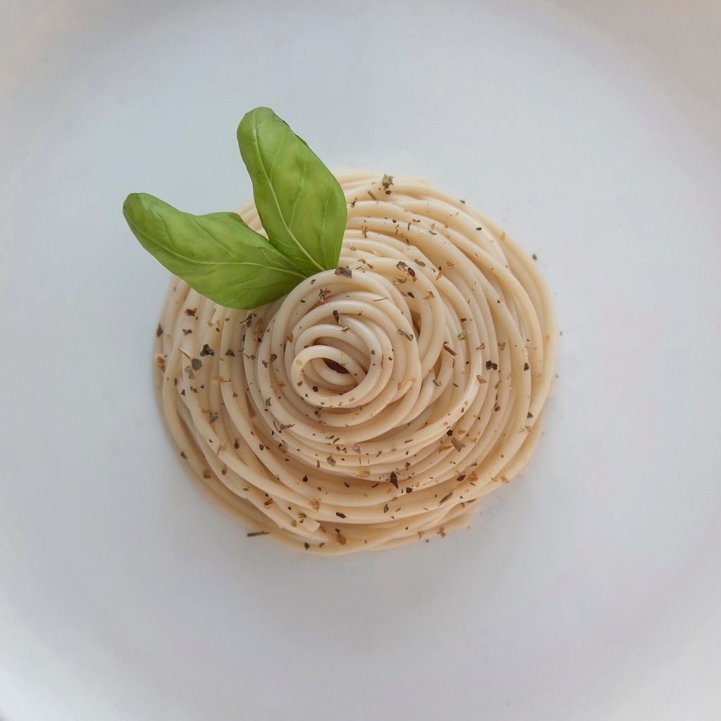 Спагетти с листьями базилика на белой тарелке