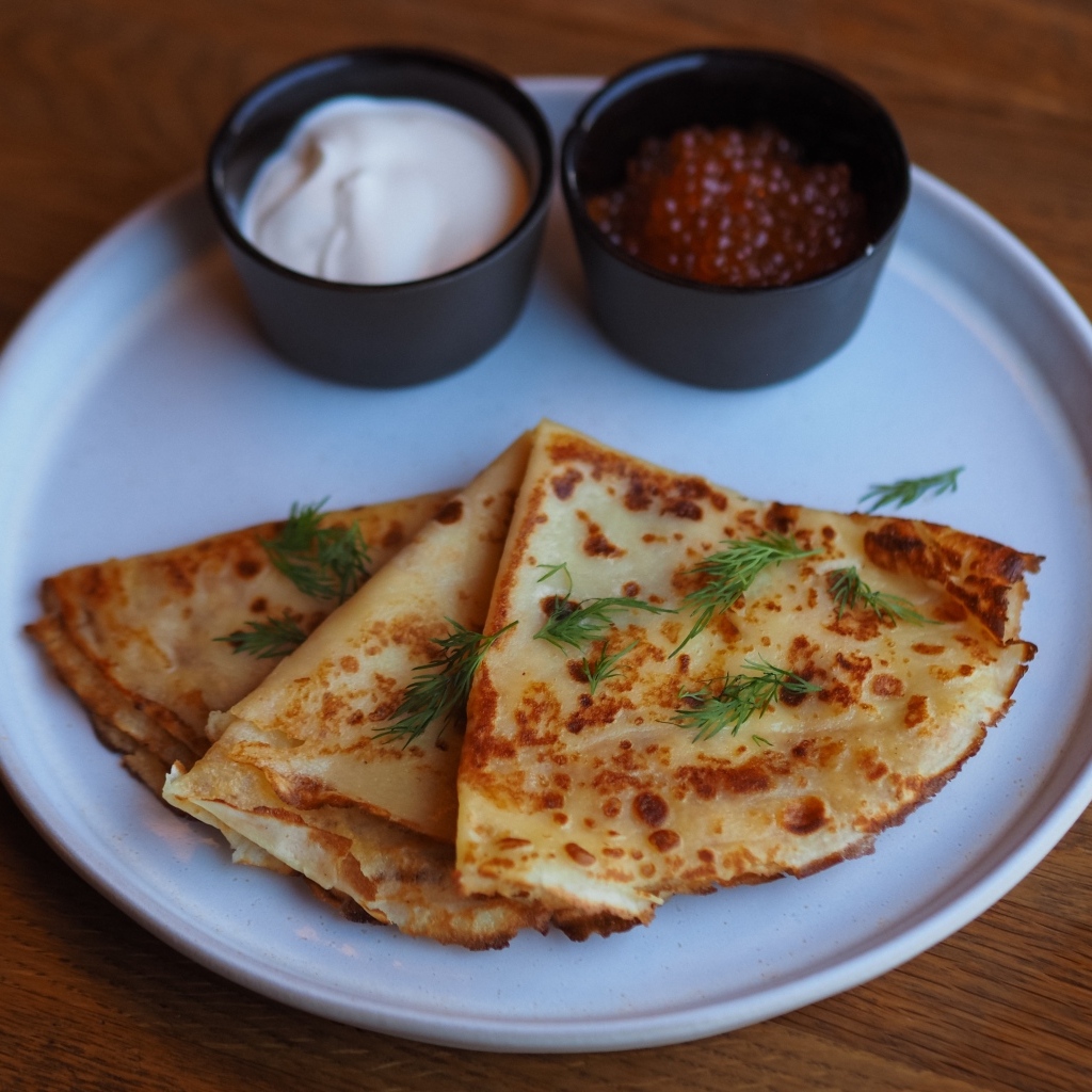 Тонкие блинчики на тарелке с красной икрой и сметаной