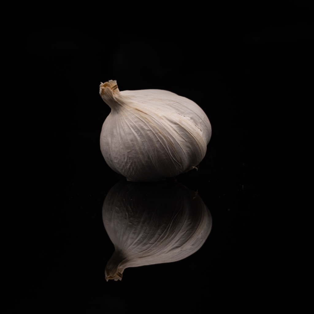 Белый чеснок отражается в черной зеркальной поверхности 
