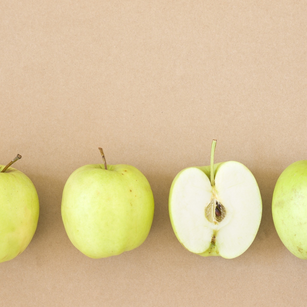 Четыре зеленых яблока на бежевом фоне 