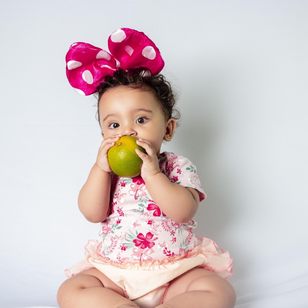 Девочка с большим бантом на голове ест апельсин