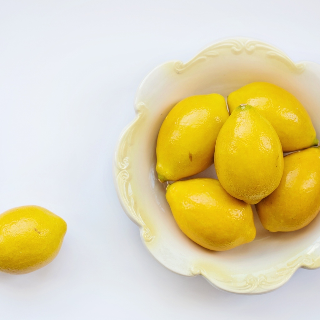 Крупные желтые лимоны в тарелке на белом фоне