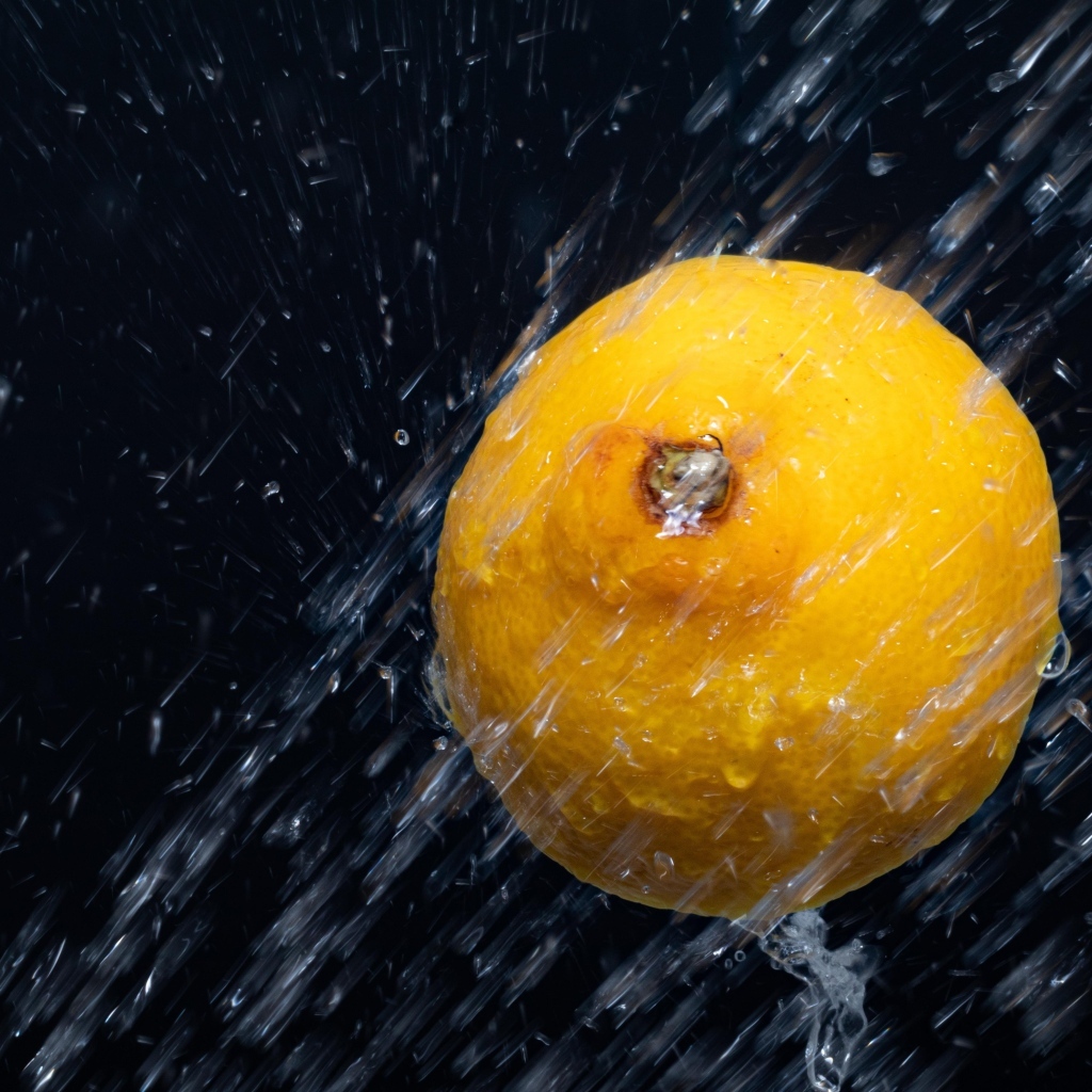 Лимон в брызгах воды на черном фоне