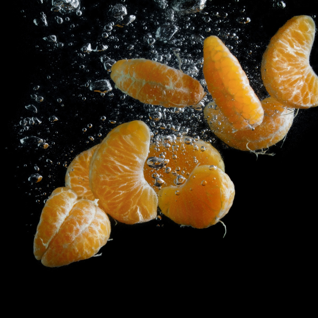 Дольки мандарина в воде на черном фоне