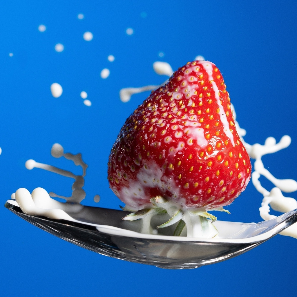 Молоко в ложке с клубникой на синем фоне