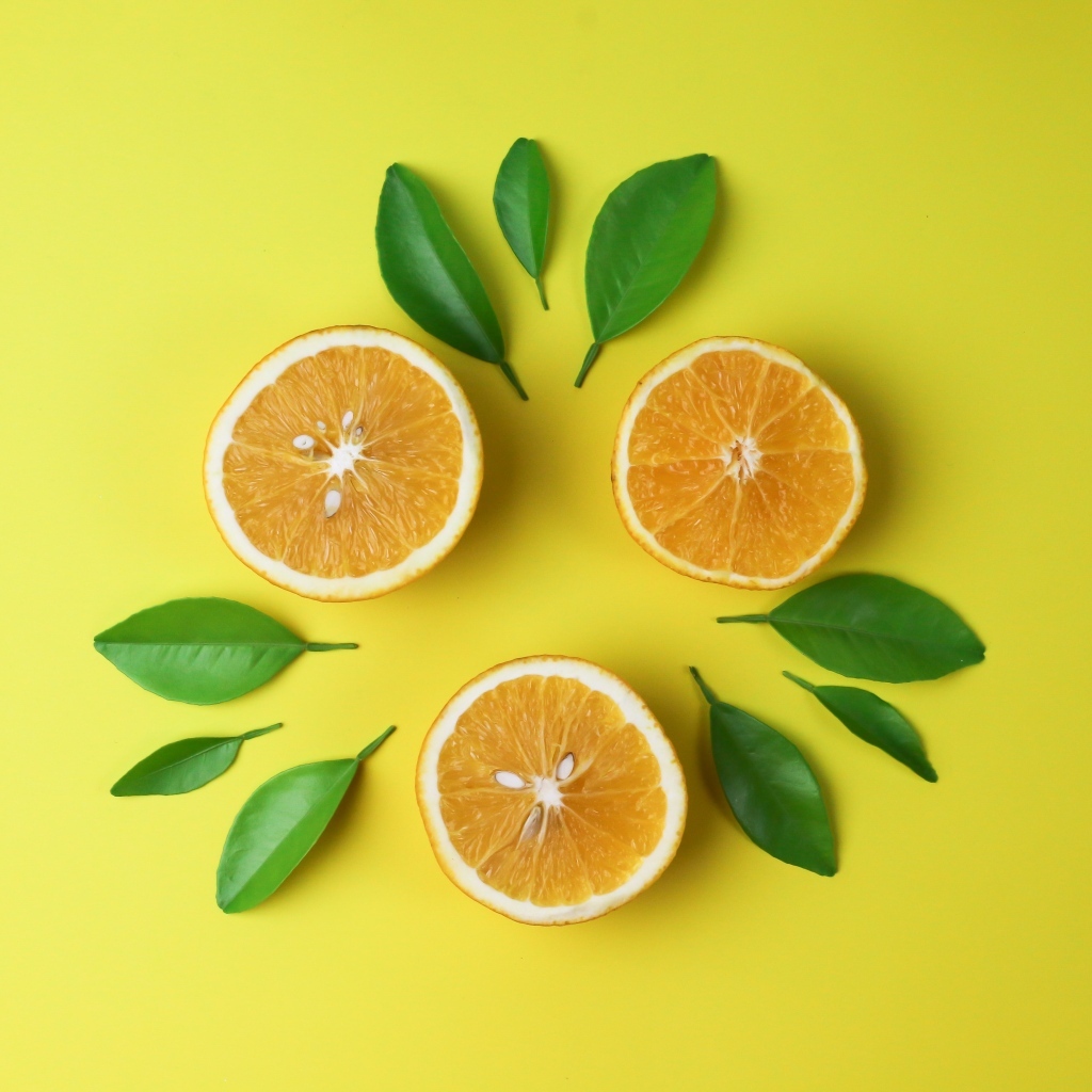 Половинки апельсина с зелеными листьями на желтом фоне