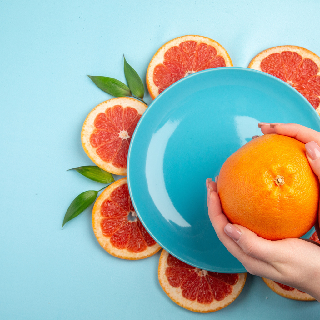 Апельсин в руках девушки на голубом фоне с тарелкой