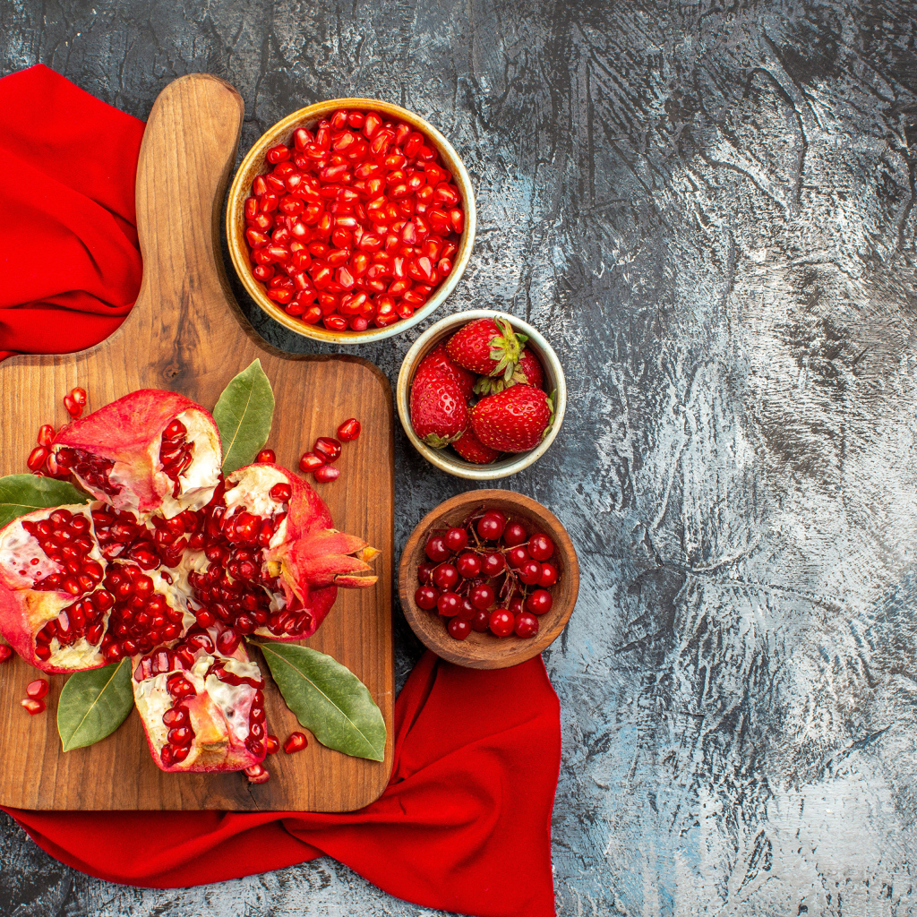 Очищенный гранат на столе с клубникой и ягодами смородины
