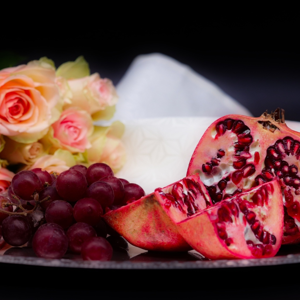 Гранат с виноградом на столе с букетом роз 