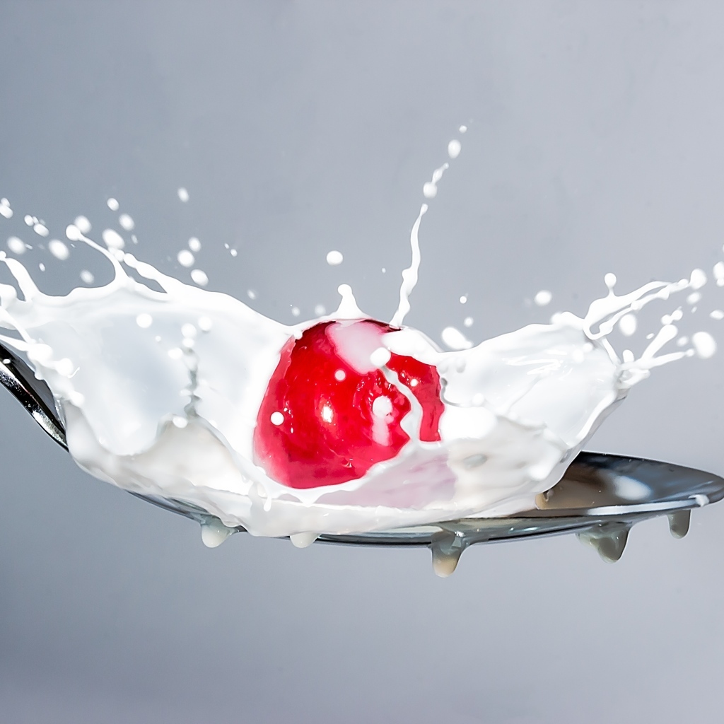 Красная черешня в ложке с молоком на сером фоне