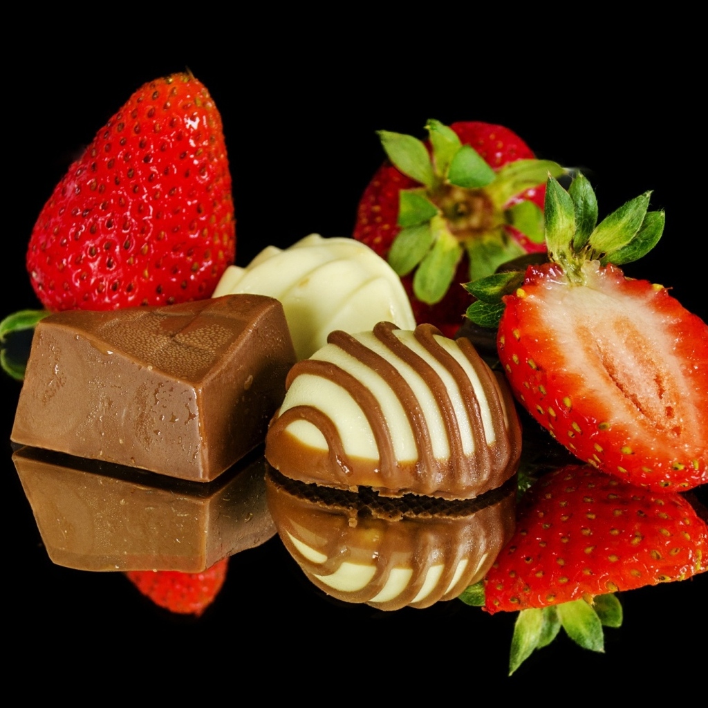 Красная клубника с шоколадными конфетами на черном фоне