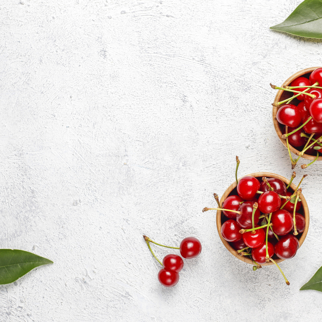 Спелая красная вишня с зелеными листьями на столе