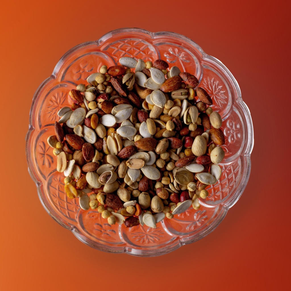 Разные орехи в стеклянной посуде на оранжевом фоне