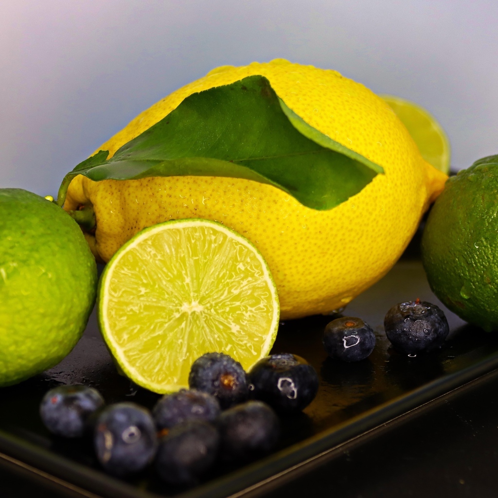 Желтый лимон на тарелке с лаймом и ягодами черники 