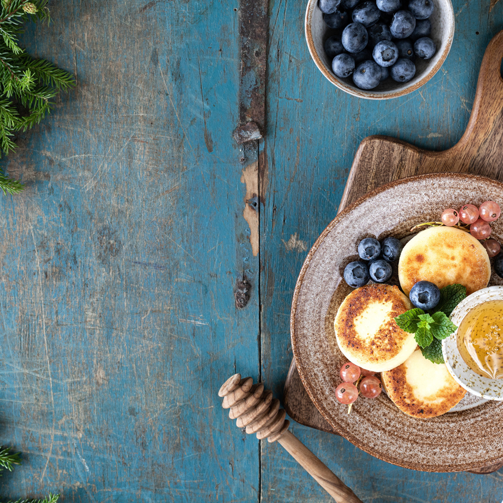 Сырники с ягодами черники на тарелке с медом