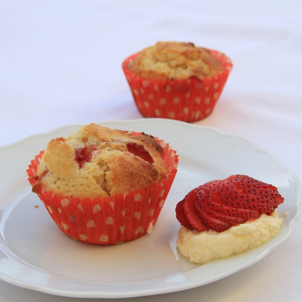 Кекс на большой белой  тарелке с кремом и клубникой