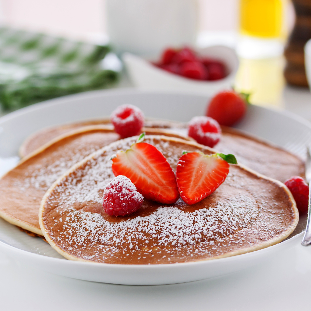 Оладьи на тарелке с сахарной пудрой и ягодами клубники