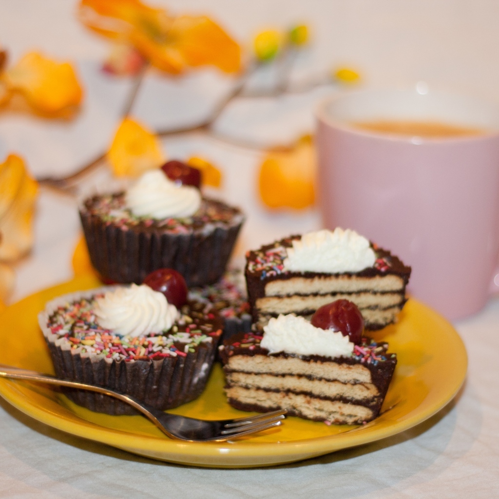 Сладкие вкусные пирожные на столе с чашкой чая и цветами