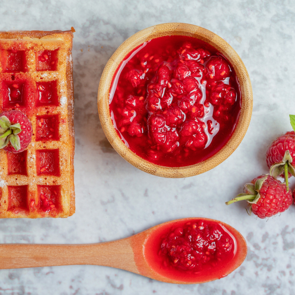 Сладкие вафли с малиновым вареньем и ягодами на столе