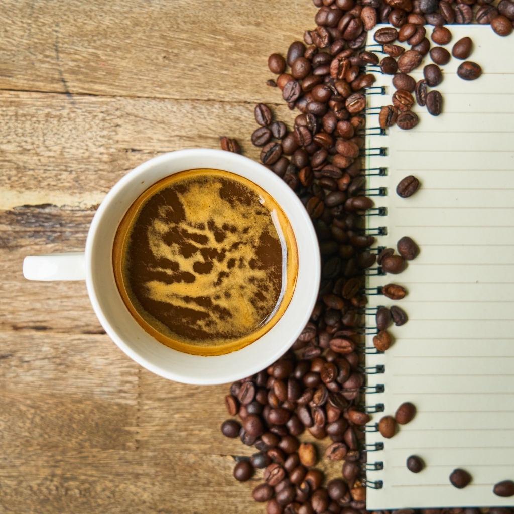 Чашка кофе на столе с зернами и блокнотом